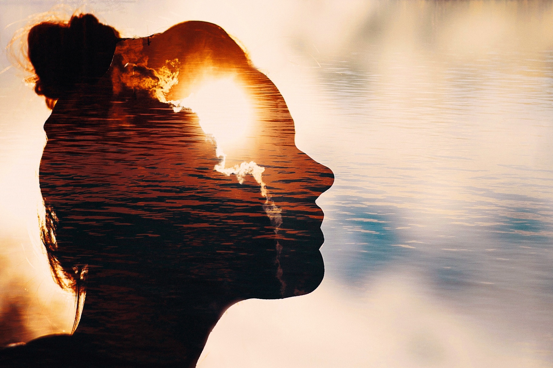 Silhouette of a woman at sunset by the water, symbolizing reflection and mental wellness